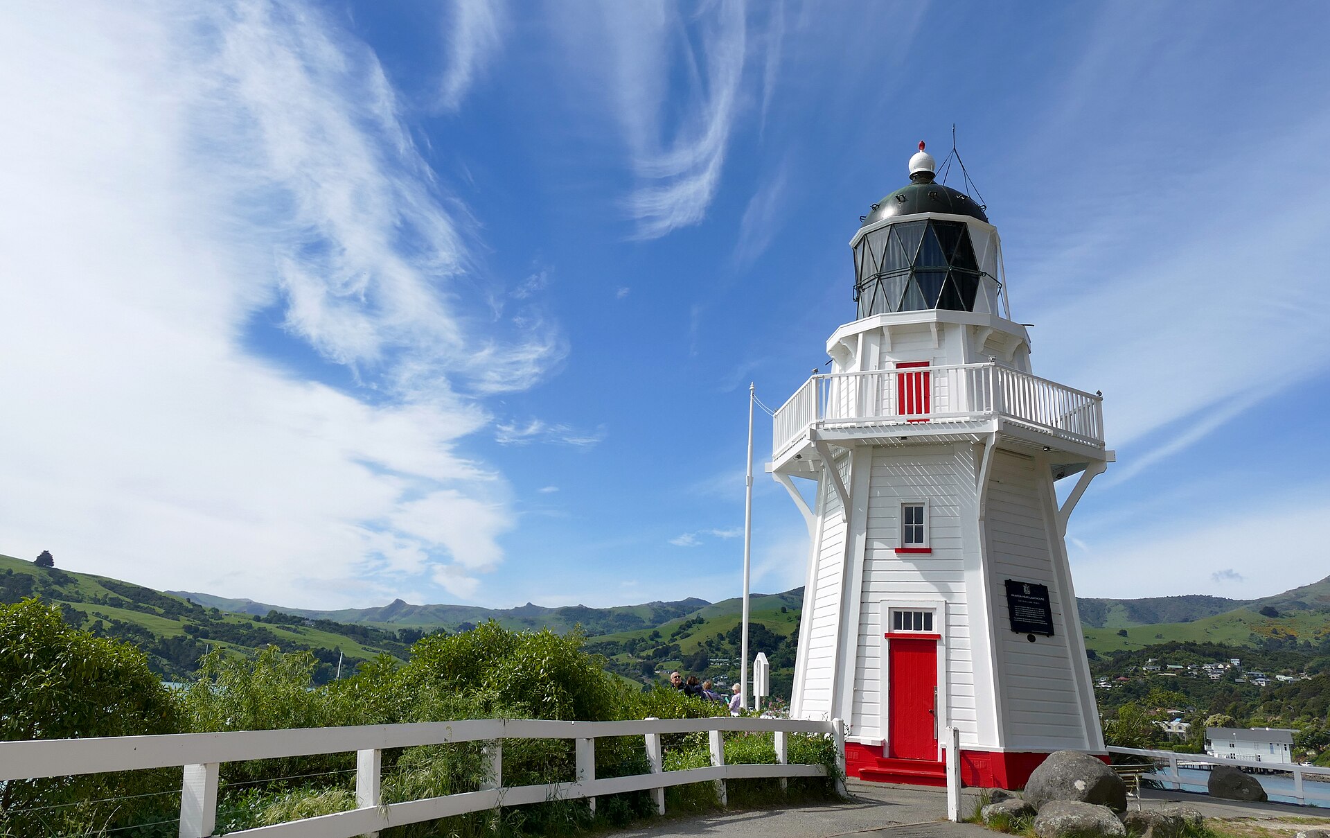 A white wooden lighthouse with red trim standing above the sea on a sunny day