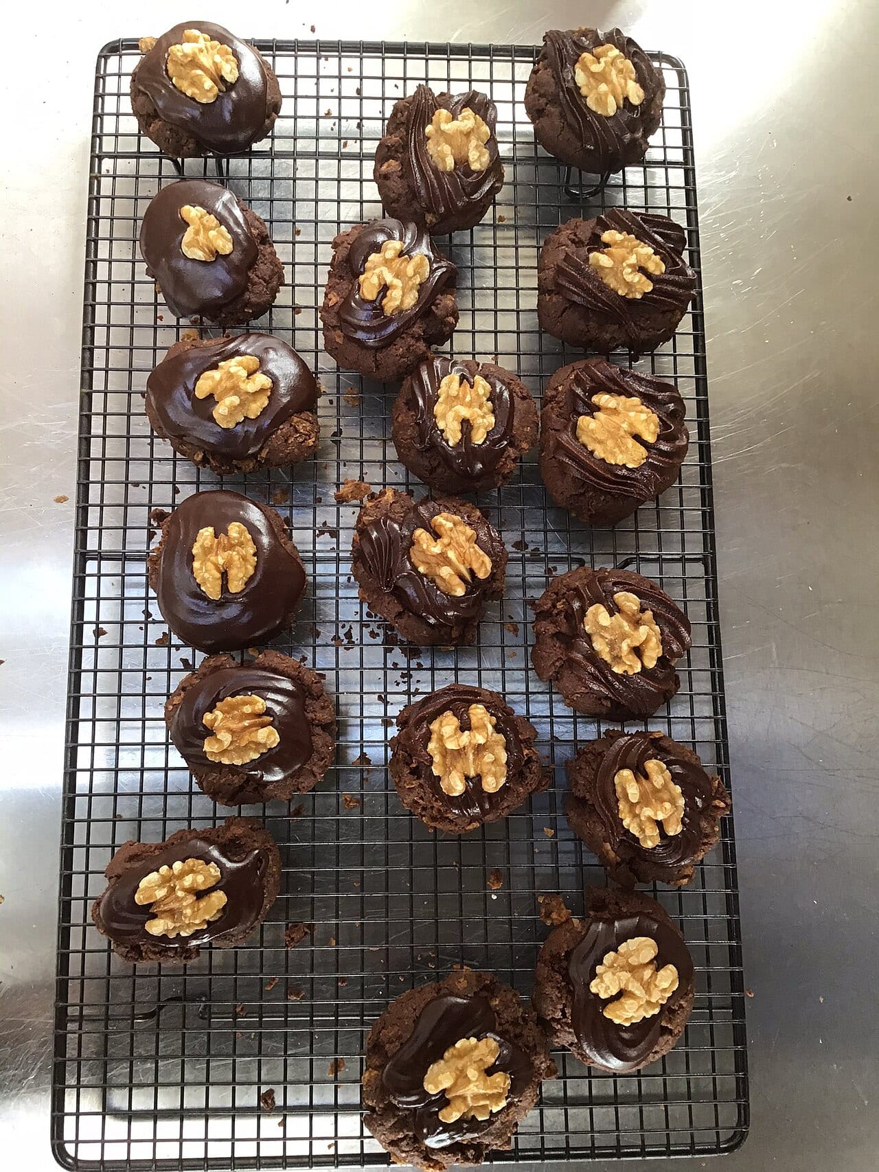 Eighteen Afghan biscuits cooling on a wire rack, each topped with chocolate icing and a walnut half.