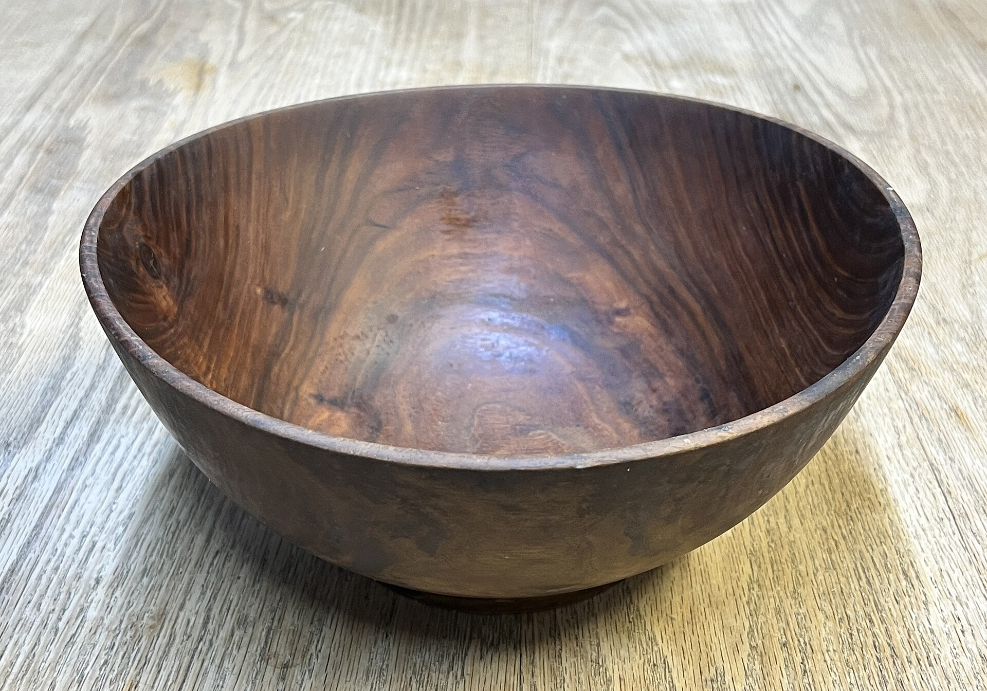 A hand-turned walnut bowl with deep swirling grain, sitting on a pale wooden table.