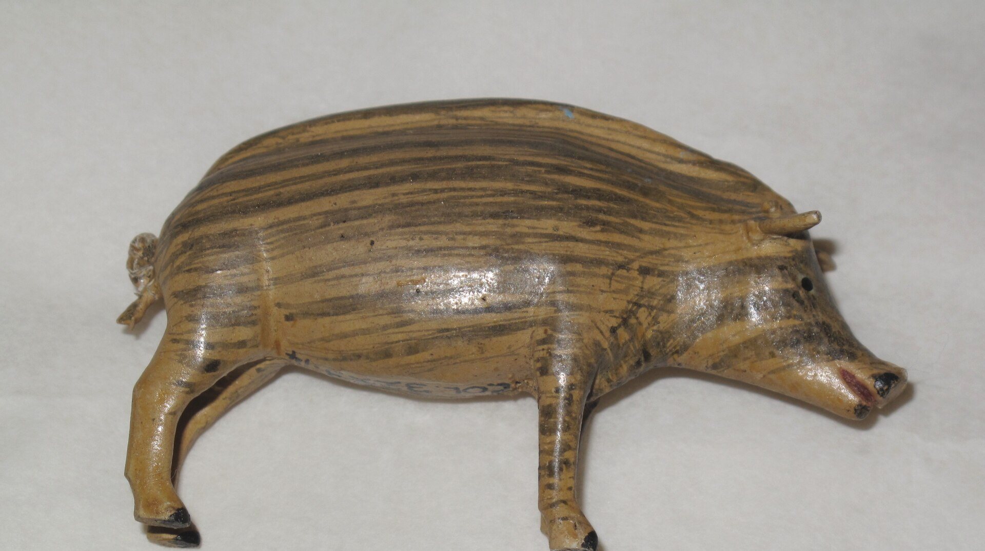 A small carved and painted toy pig with striped markings, standing on a plain white surface.